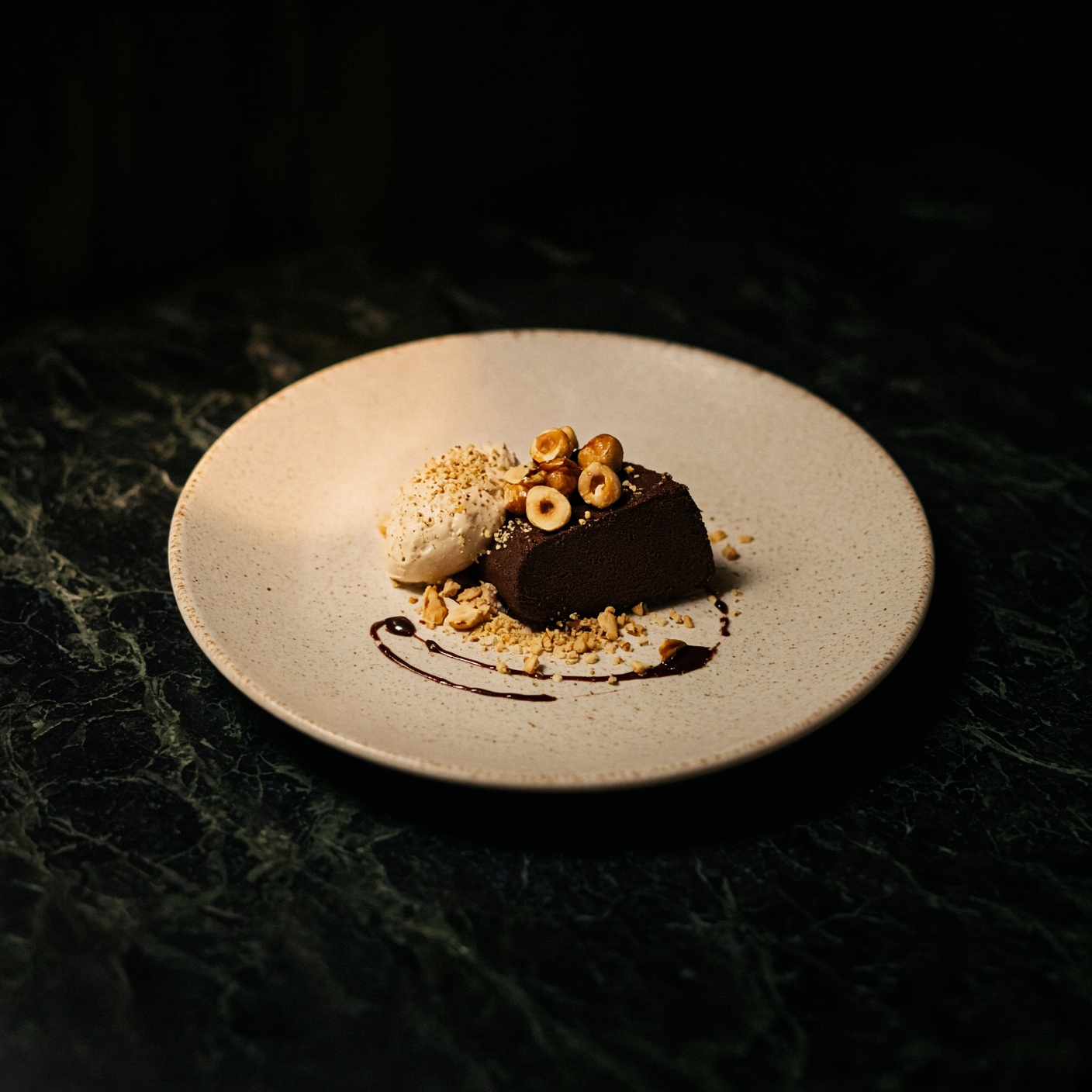 A slice of dark chocolate terrine with candied hazelnuts and cream on a speckled cream plate.