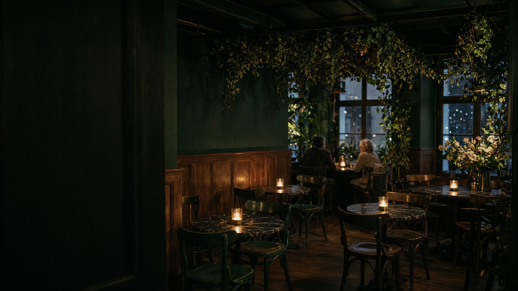 The dining room at night: bentwood chairs, small marble tables, candles on every table, greenery and flowers hung through the room.
